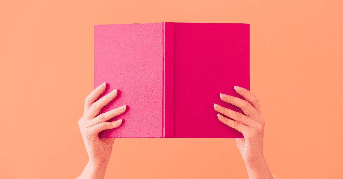 Storytelling in Content Creation for Stronger Brand Messaging 1 Hands holding up a pink book on an orange background to give contect to storytelling in content creation