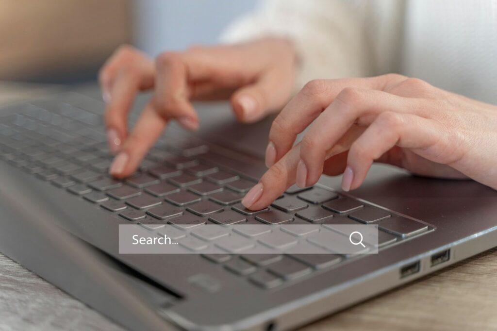 A lady types on a laptop keyboard with a graphic of a search bar over the image.